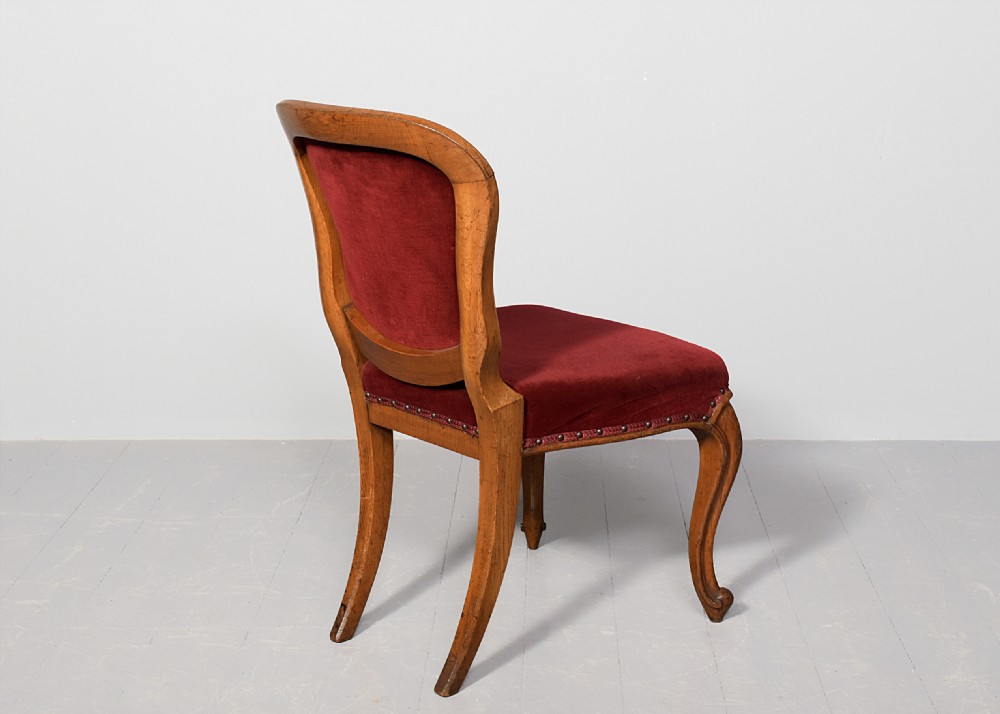 A set of twelve French carved oak dining chairs with balloon backs, cabriole legs, and red velvet or patterned fabric upholstery. View V