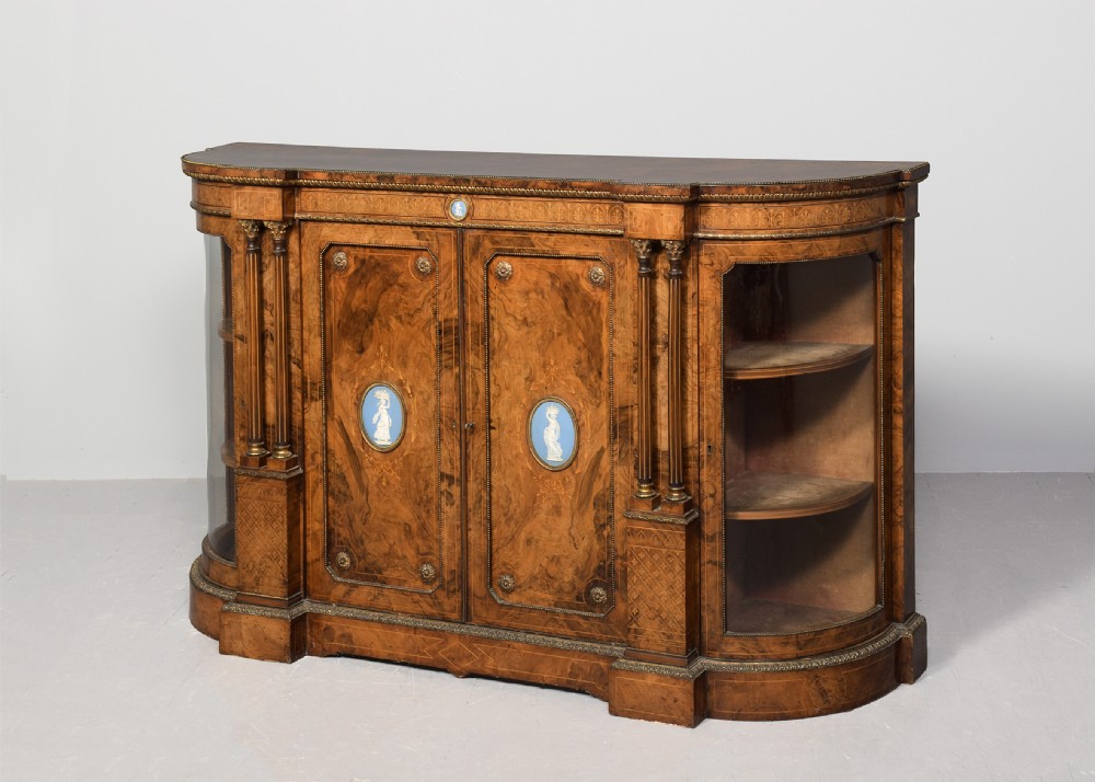 A Victorian burr walnut credenza featuring curved glazed end display sections, twin central cupboard doors decorated with blue Jasperware plaques, and gilt metal mounts.