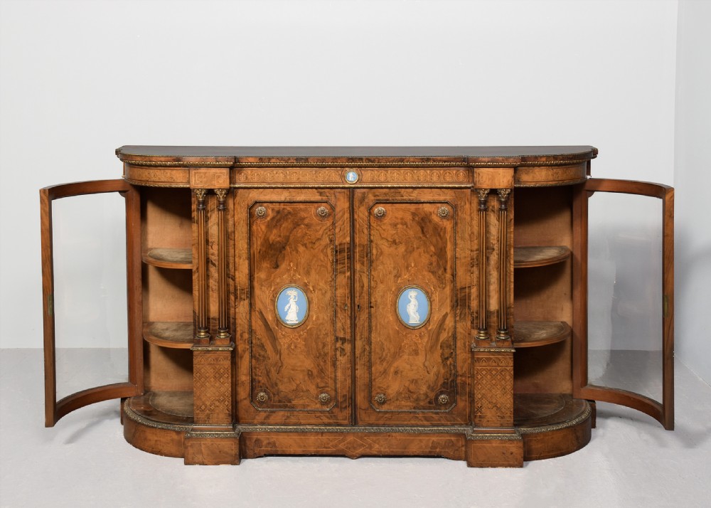A Victorian burr walnut credenza featuring curved glazed end display sections, twin central cupboard doors decorated with blue Jasperware plaques, and gilt metal mounts. View IX