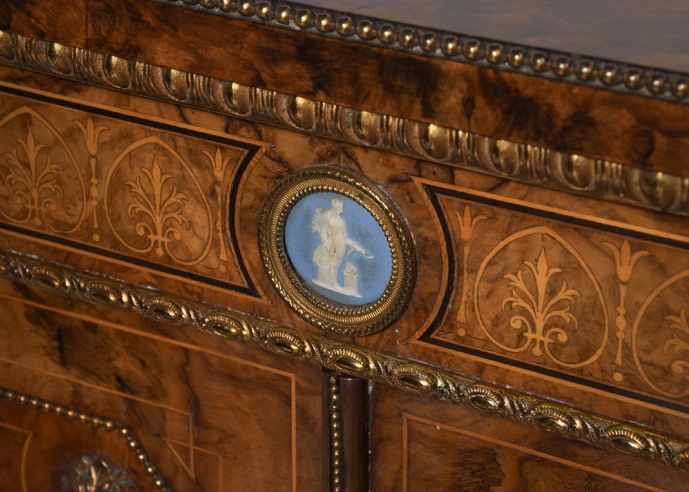 A Victorian burr walnut credenza featuring curved glazed end display sections, twin central cupboard doors decorated with blue Jasperware plaques, and gilt metal mounts. View XI