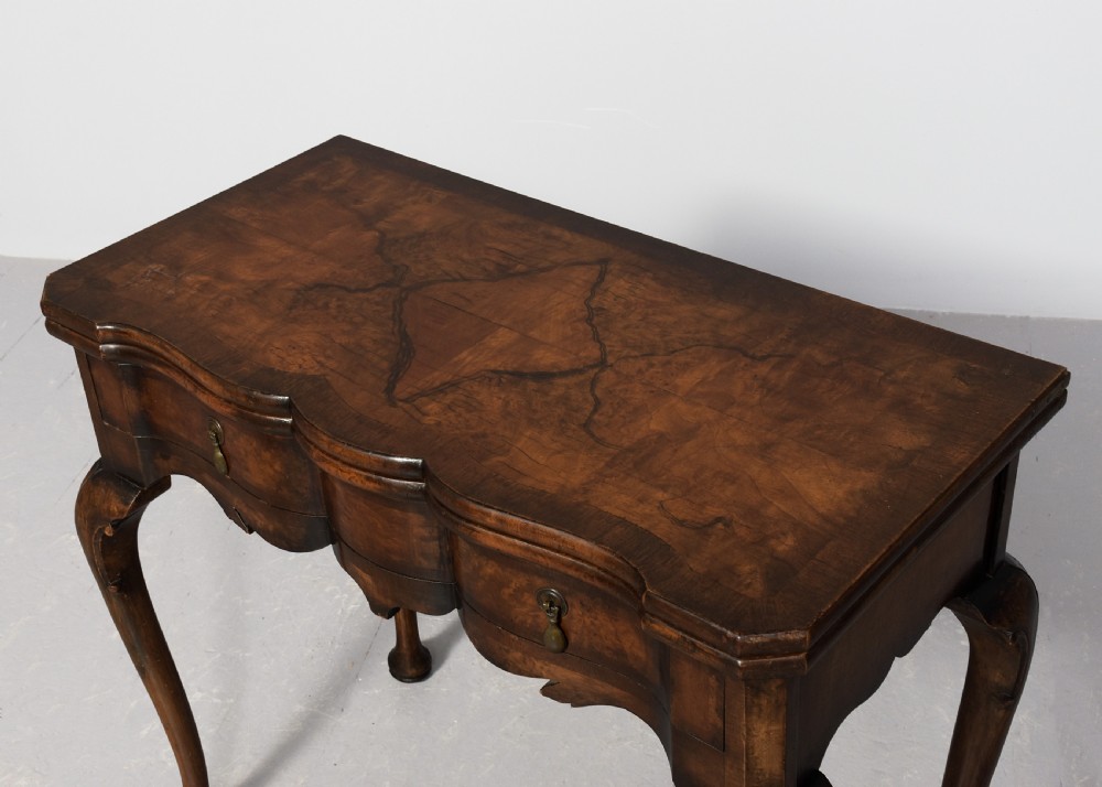 An early Georgian style fold-over walnut games table featuring a shaped top, frieze drawers with brass drop handles, and cabriole legs on pad feet. View II