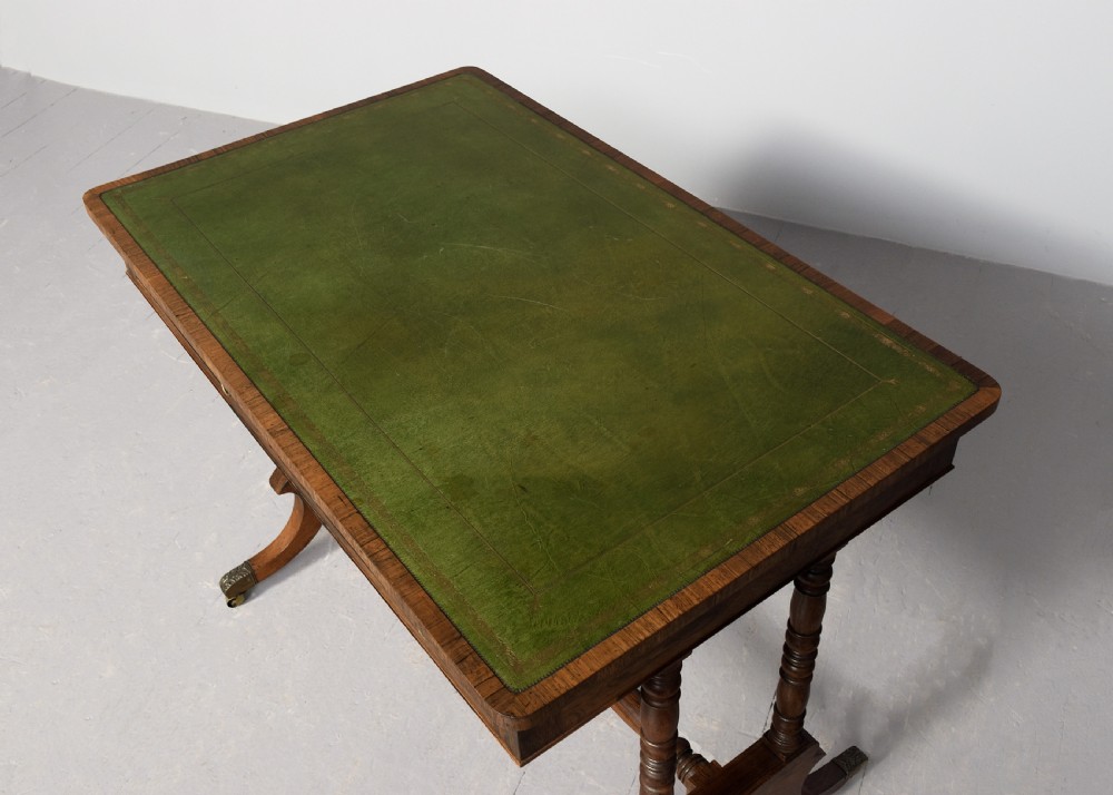 A Regency rosewood library table featuring a green leather insert top, two drawers with brass ring handles, turned supports, and splayed legs with brass castors. View III
