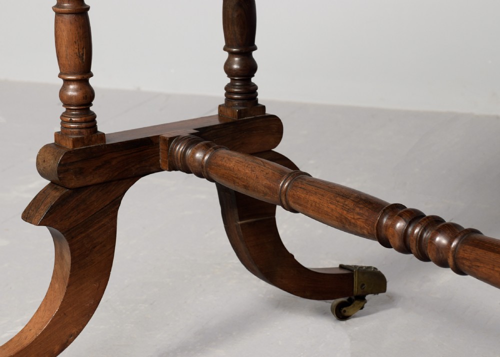A Regency rosewood library table featuring a green leather insert top, two drawers with brass ring handles, turned supports, and splayed legs with brass castors. View V