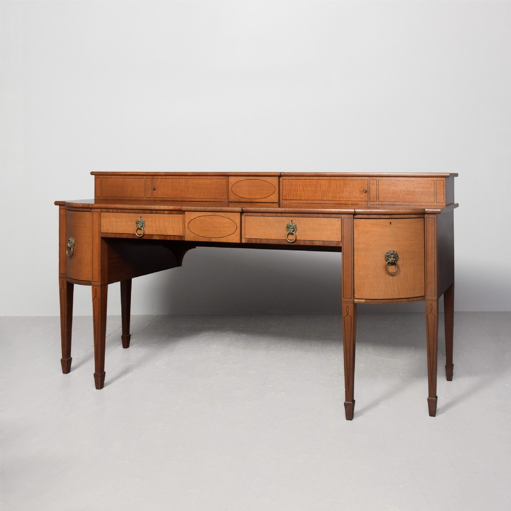 A George III mahogany stage-back sideboard featuring a raised upper tier, oval inlay detailing, brass lion-mask ring pulls, and tapered square legs.