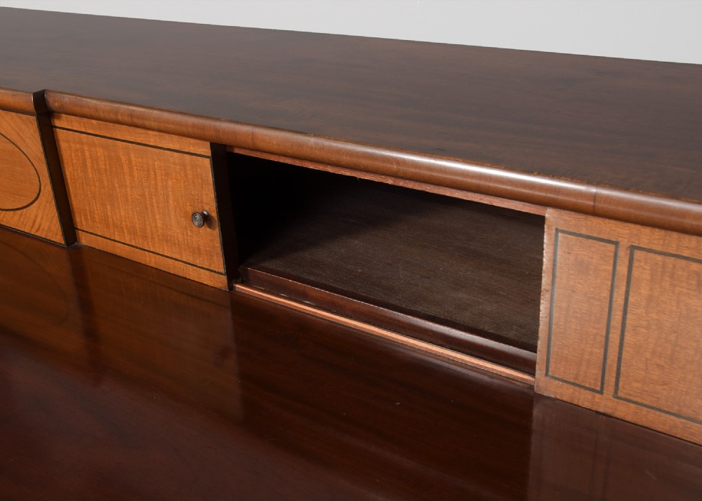 A George III mahogany stage-back sideboard featuring a raised upper tier, oval inlay detailing, brass lion-mask ring pulls, and tapered square legs. View IV