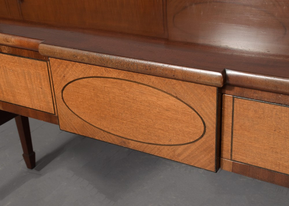 A George III mahogany stage-back sideboard featuring a raised upper tier, oval inlay detailing, brass lion-mask ring pulls, and tapered square legs. View VIII