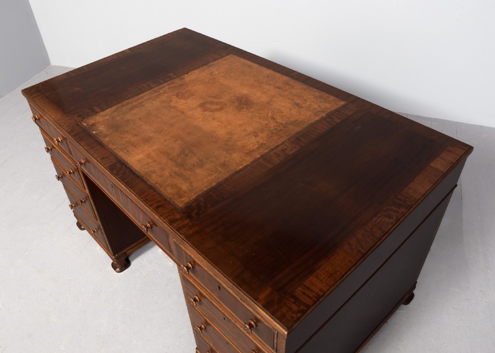 A mahogany three-part pedestal desk featuring a three-panel leather inset top, flame mahogany drawer fronts, turned wooden knobs, and bracket feet. View IV