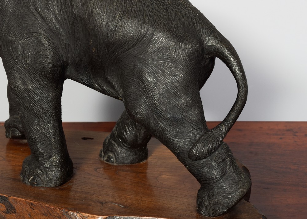 A dark patinated Japanese bronze elephant sculpture with raised trunk and white tusks, mounted on a naturalistic cut wood base. View V