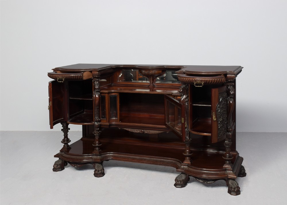 A late Victorian dark mahogany sideboard featuring detailed carved relief cupboard doors, a central glazed cabinet, mirrored back panel, and carved lion paw feet. View II