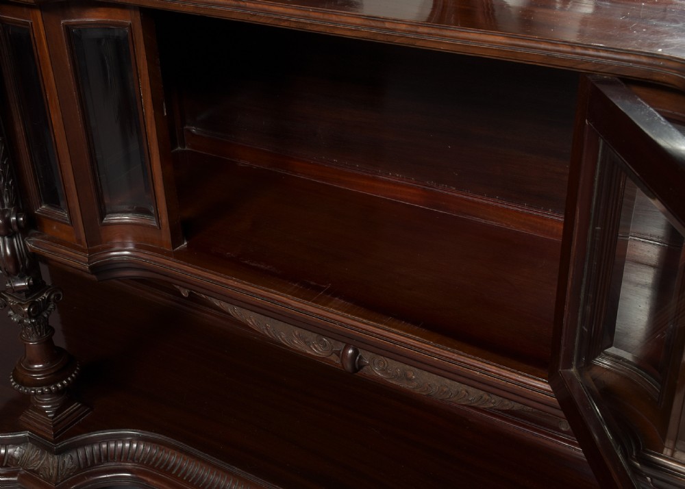 A late Victorian dark mahogany sideboard featuring detailed carved relief cupboard doors, a central glazed cabinet, mirrored back panel, and carved lion paw feet. View III