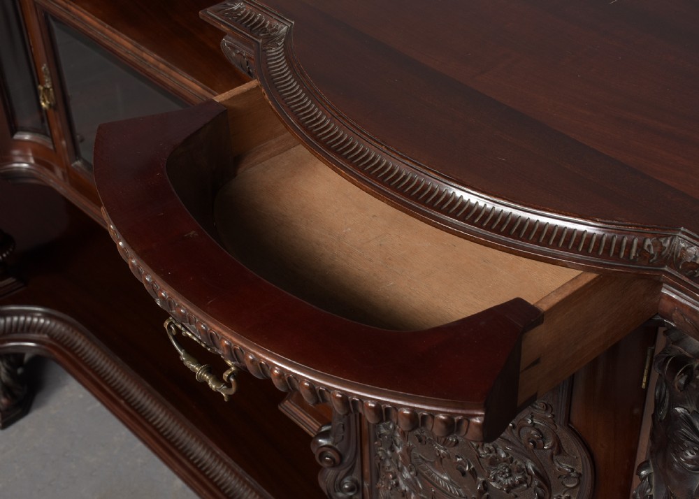 A late Victorian dark mahogany sideboard featuring detailed carved relief cupboard doors, a central glazed cabinet, mirrored back panel, and carved lion paw feet. View IV