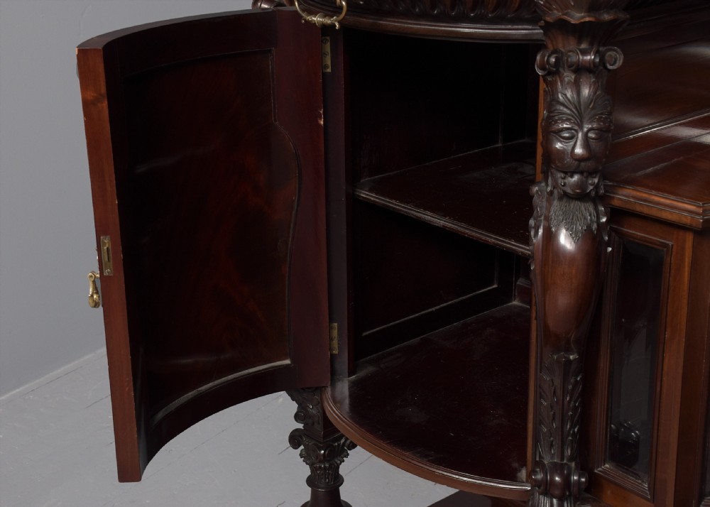 A late Victorian dark mahogany sideboard featuring detailed carved relief cupboard doors, a central glazed cabinet, mirrored back panel, and carved lion paw feet. View V