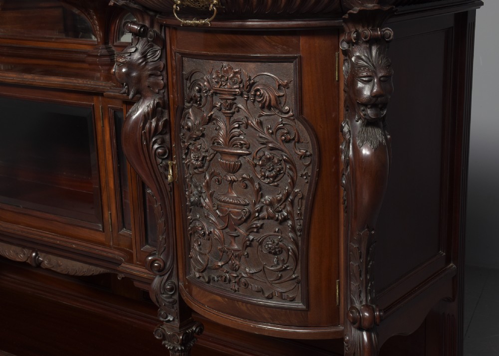 A late Victorian dark mahogany sideboard featuring detailed carved relief cupboard doors, a central glazed cabinet, mirrored back panel, and carved lion paw feet. View VIII
