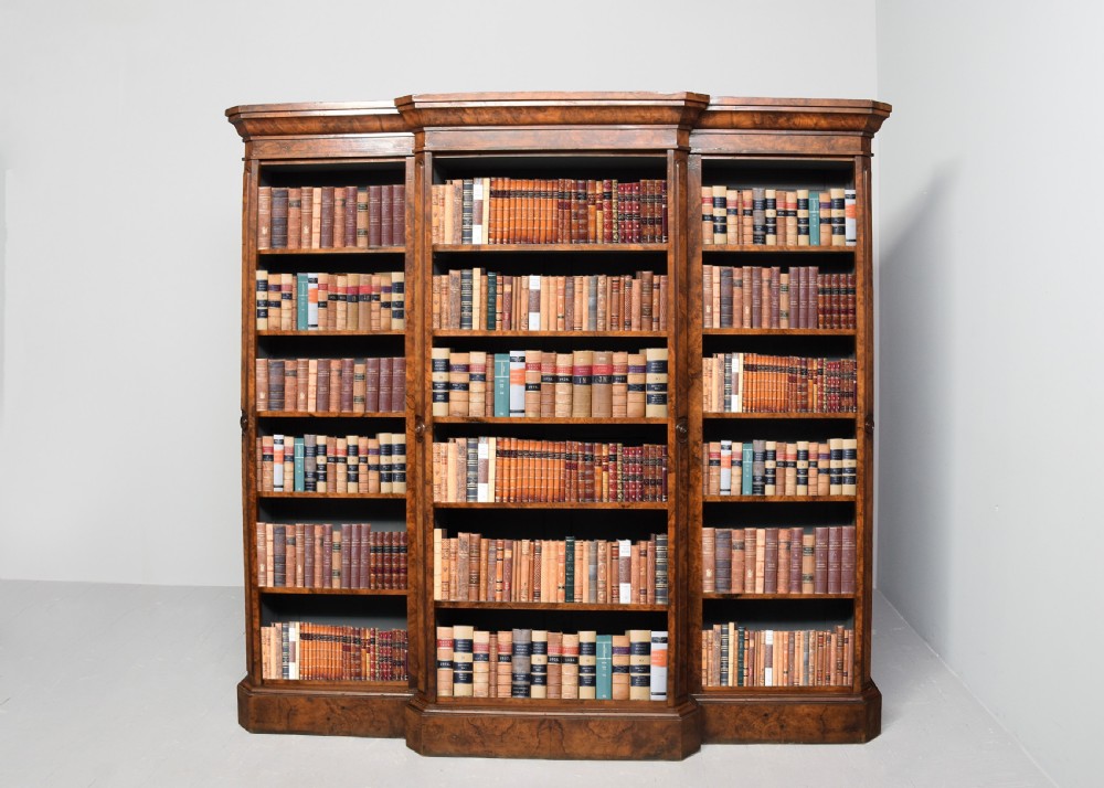 A large three-section Victorian open bookcase made from burr walnut with a breakfront centre section, adjustable shelves, and a plinth base.