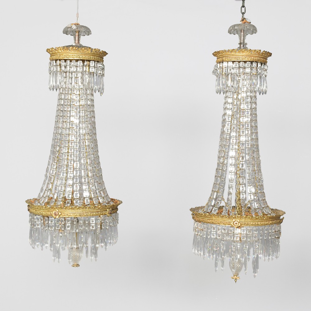 A pair of matching tall crystal and gilt brass chandeliers featuring tapered bead strands, ornate metal coronets, and hanging prism drops.