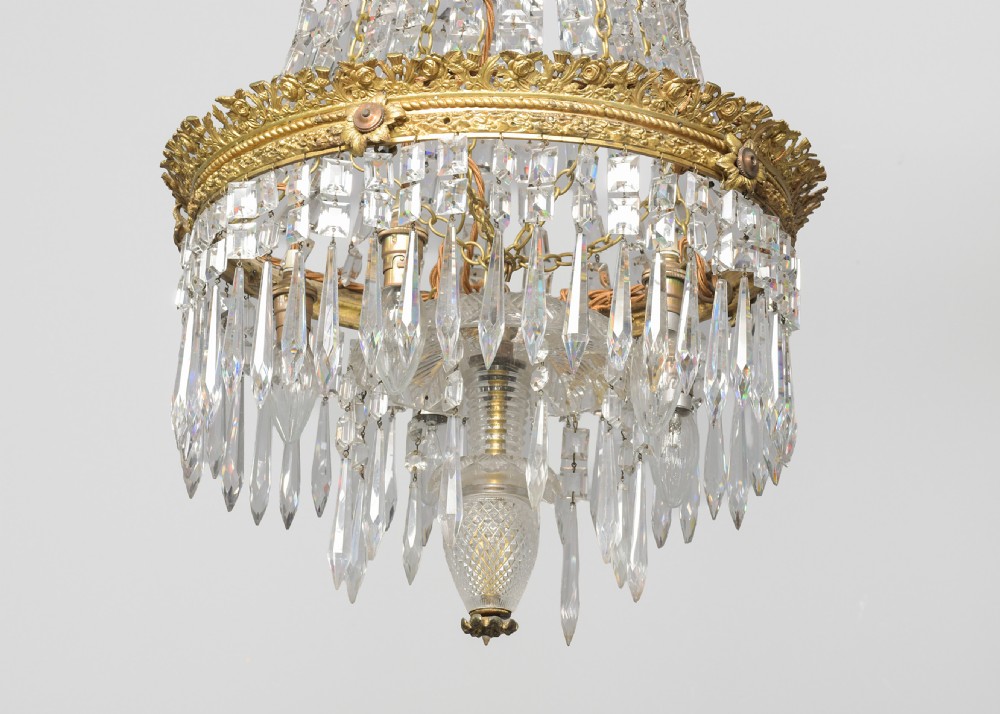A pair of matching tall crystal and gilt brass chandeliers featuring tapered bead strands, ornate metal coronets, and hanging prism drops. View VI