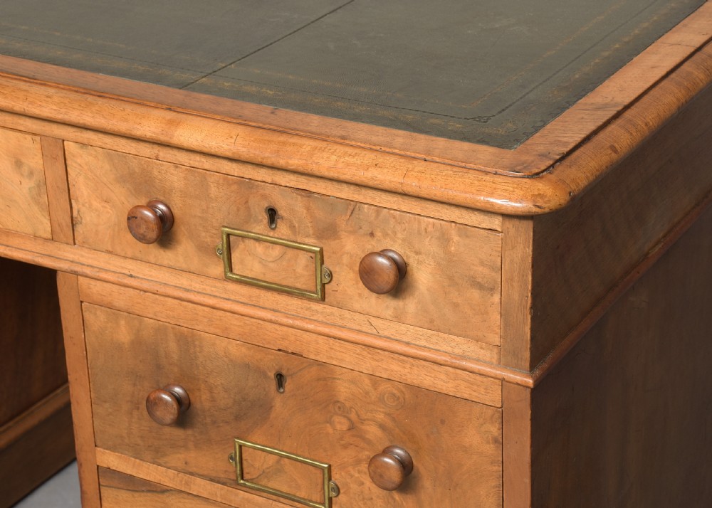 Victorian figured walnut pedestal desk featuring a green gilt-tooled leather writing surface, multiple drawers with turned wooden knobs, brass card handles, and plinth bases. View II