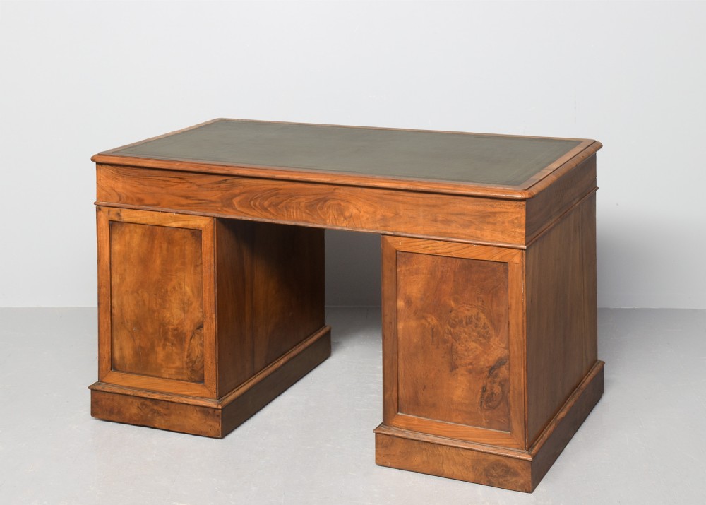 Victorian figured walnut pedestal desk featuring a green gilt-tooled leather writing surface, multiple drawers with turned wooden knobs, brass card handles, and plinth bases. View VII