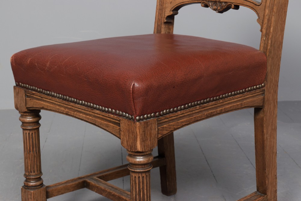 A set of twelve Victorian oak dining chairs upholstered in rich brown leather with brass stud details and turned legs on castors. View X