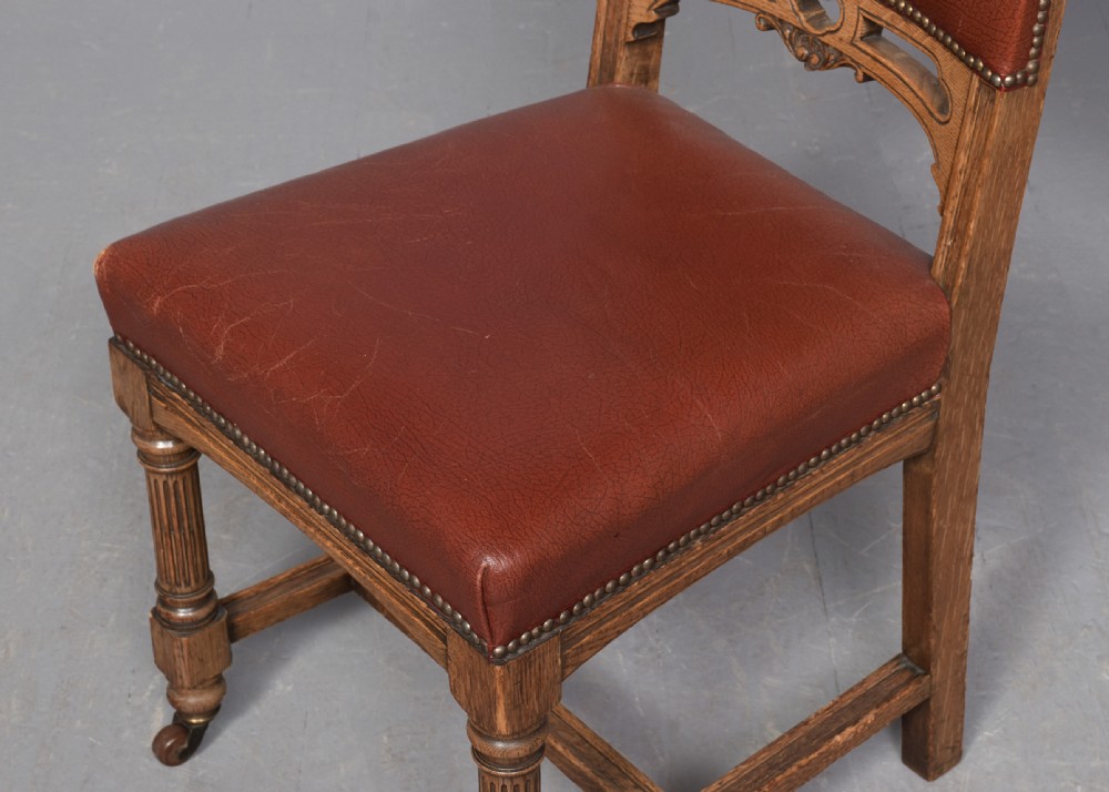 A set of twelve Victorian oak dining chairs upholstered in rich brown leather with brass stud details and turned legs on castors. View XI
