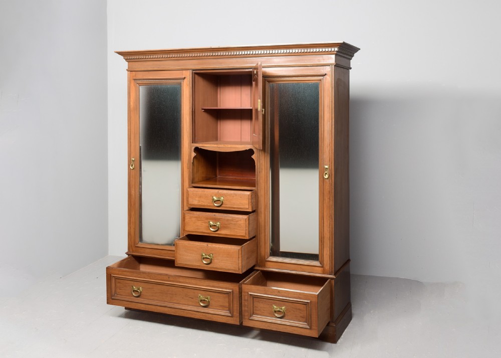 A straight-grained walnut three-section wardrobe with two tall mirrored doors flanking a central column containing a small cupboard, open shelf, and multiple drawers. View VI
