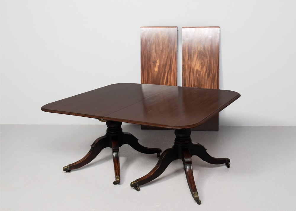 An extended George IV mahogany dining table featuring two turned pedestal supports with splayed legs, brass castors, and two removable leaf sections. View V