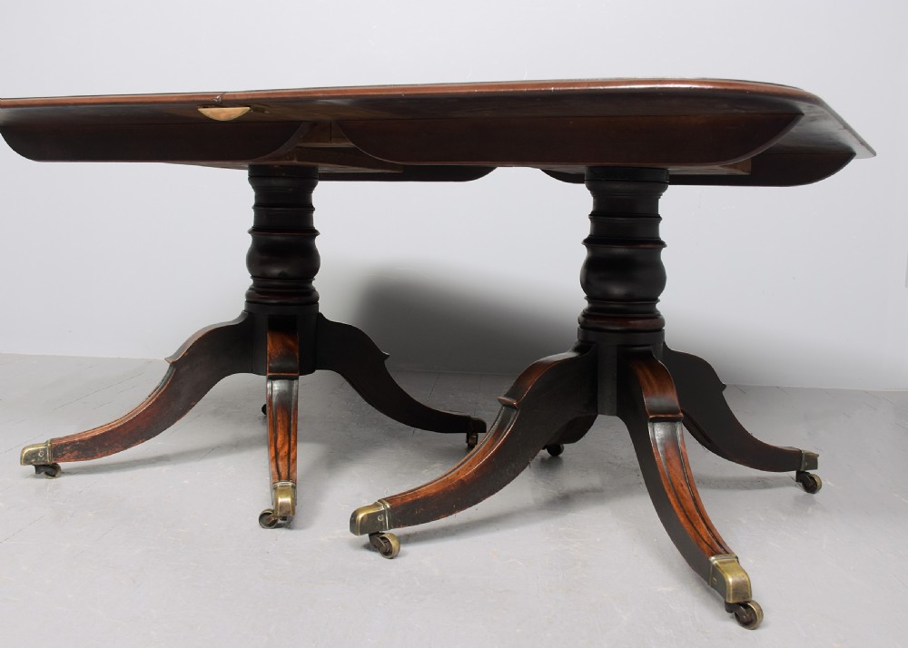 An extended George IV mahogany dining table featuring two turned pedestal supports with splayed legs, brass castors, and two removable leaf sections. View VI