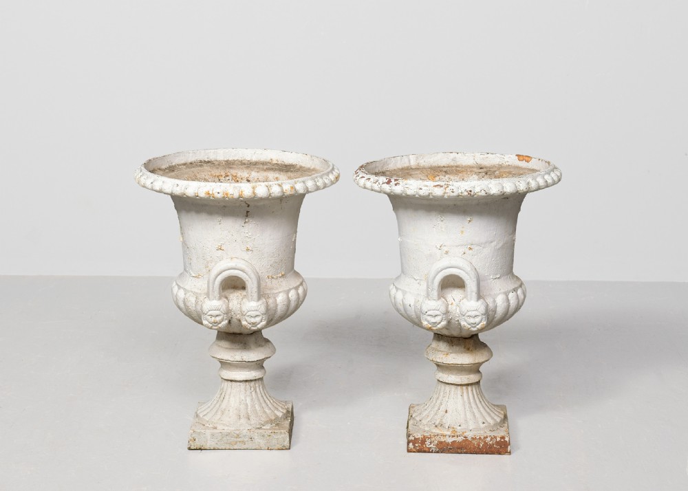 A pair of classical off-white painted cast iron Campagna urns featuring gadrooned rims, looped handles, and square pedestal bases displaying surface rust and patination. View VII