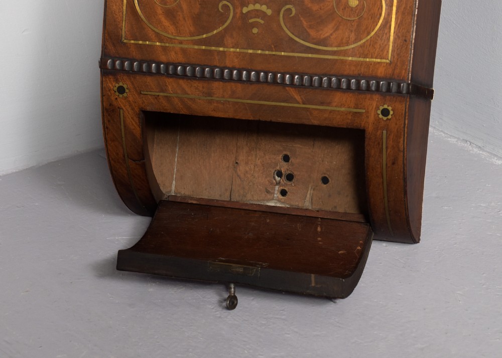 An antique mahogany drop dial fusee wall clock featuring brass inlay decoration, a circular white dial with black Roman numerals, and an open hinged brass bezel. View IV