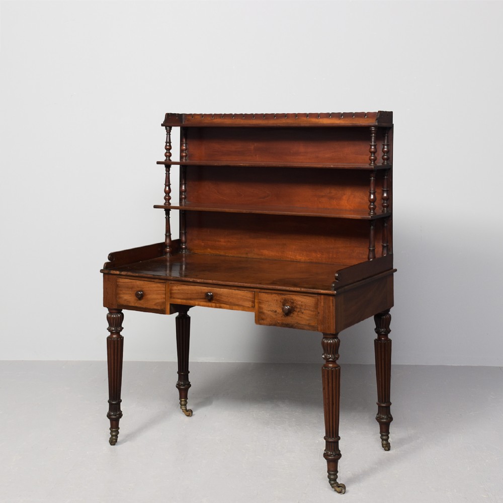 A Regency mahogany writing desk featuring a tiered shelving gallery, three frieze drawers, fluted reeded legs, and brass castors.