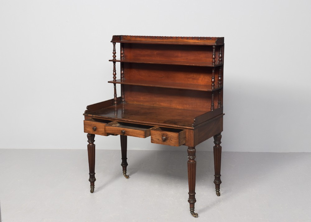A Regency mahogany writing desk featuring a tiered shelving gallery, three frieze drawers, fluted reeded legs, and brass castors. View II