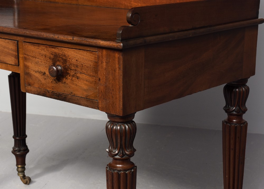 A Regency mahogany writing desk featuring a tiered shelving gallery, three frieze drawers, fluted reeded legs, and brass castors. View VII