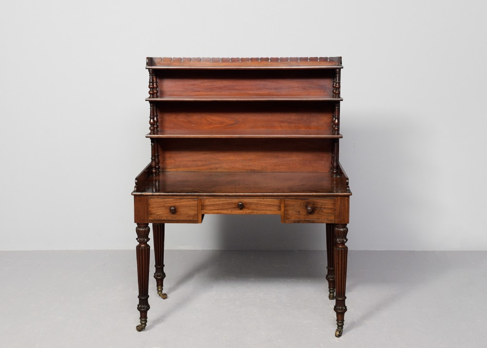 A Regency mahogany writing desk featuring a tiered shelving gallery, three frieze drawers, fluted reeded legs, and brass castors. View VIII