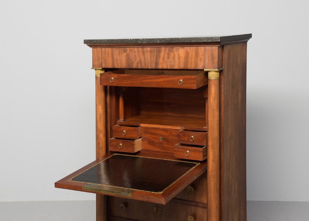 A tall mahogany secretaire abattant featuring a dark marble top, a drop-front writing panel flanked by turned columns, and three lower drawers with brass handles. View V
