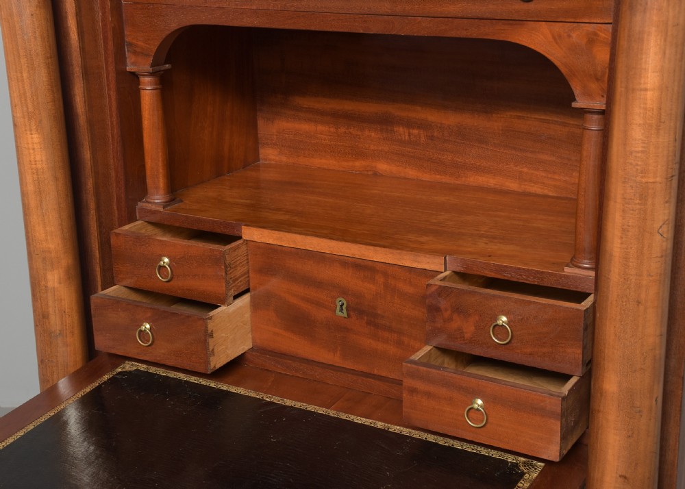 A tall mahogany secretaire abattant featuring a dark marble top, a drop-front writing panel flanked by turned columns, and three lower drawers with brass handles. View VI