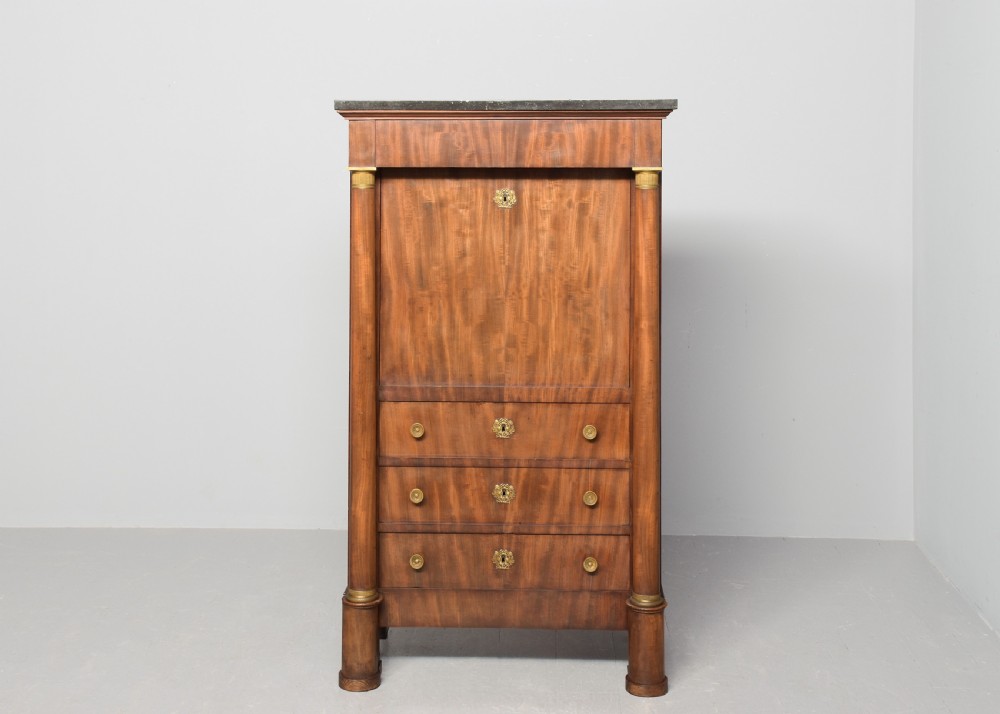 A tall mahogany secretaire abattant featuring a dark marble top, a drop-front writing panel flanked by turned columns, and three lower drawers with brass handles. View X