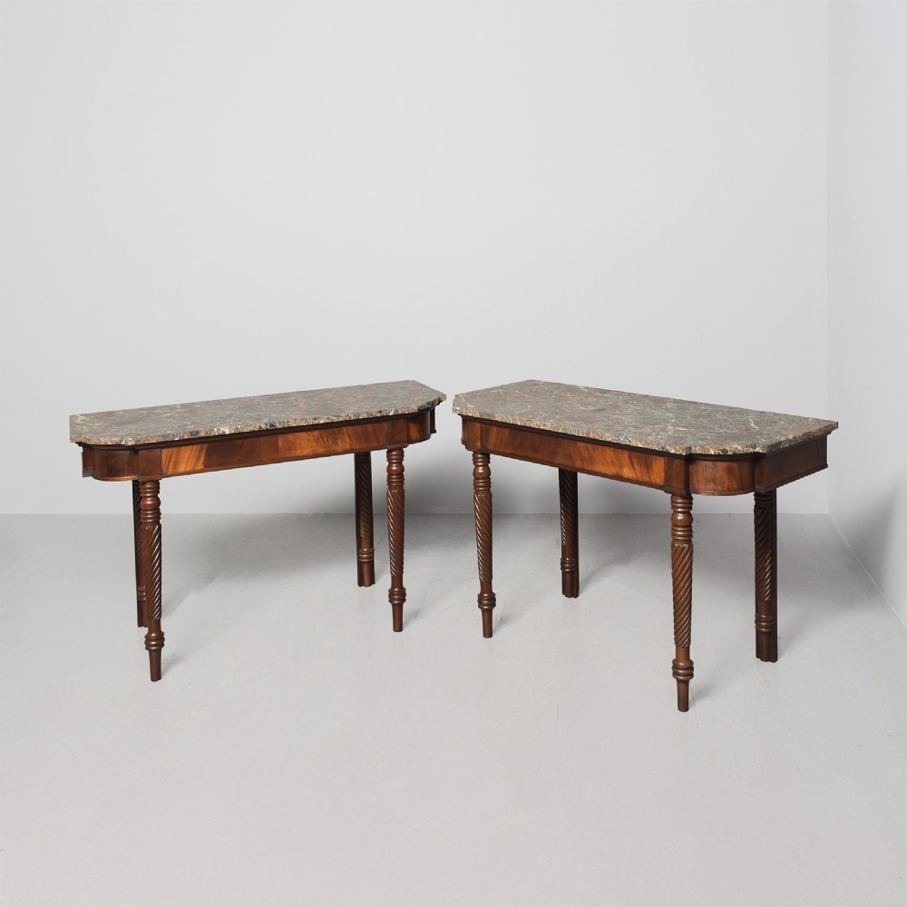 A pair of William IV mahogany break-front hall tables featuring grey marble tops and spiral-turned legs.