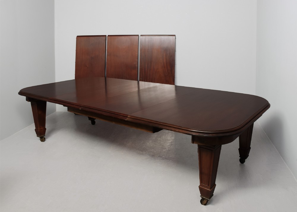 A large rectangular Victorian mahogany extending dining table featuring rounded corners, faceted tapered legs, a fifth central support leg, and brass castors. View IX