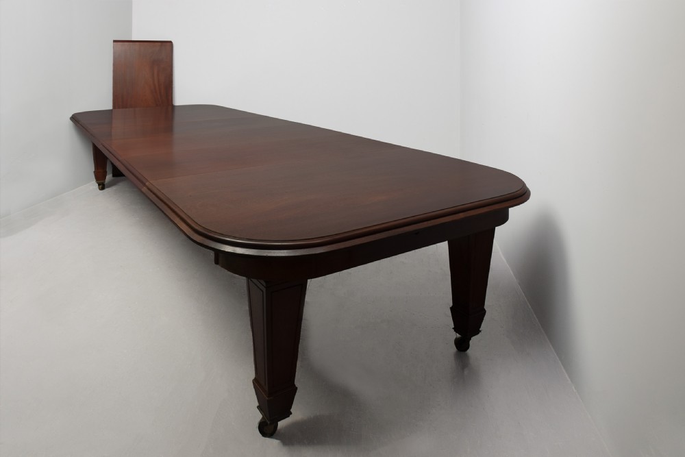A large rectangular Victorian mahogany extending dining table featuring rounded corners, faceted tapered legs, a fifth central support leg, and brass castors. View XIV