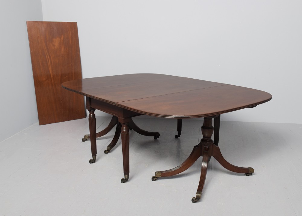 A Regency mahogany twin-pedestal extending dining table supported by reeded splayed legs with brass castors. View II