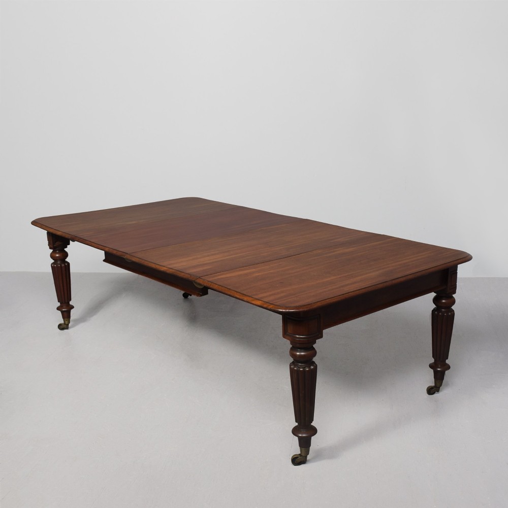 A rectangular George IV mahogany extending dining table with rounded corners, reeded turned legs, and brass castors.