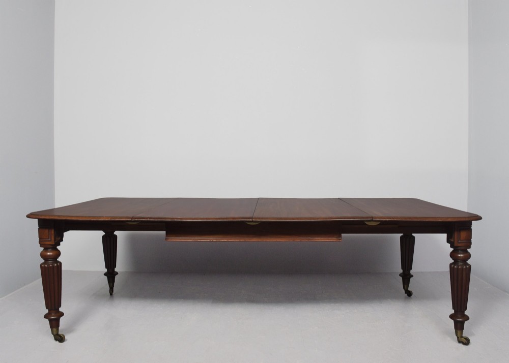 A rectangular George IV mahogany extending dining table with rounded corners, reeded turned legs, and brass castors. View II