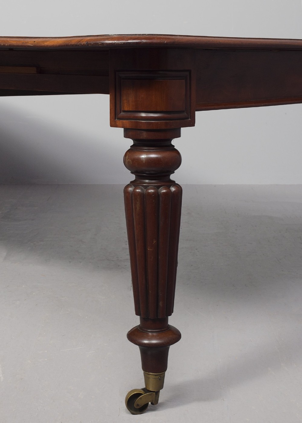 A rectangular George IV mahogany extending dining table with rounded corners, reeded turned legs, and brass castors. View III