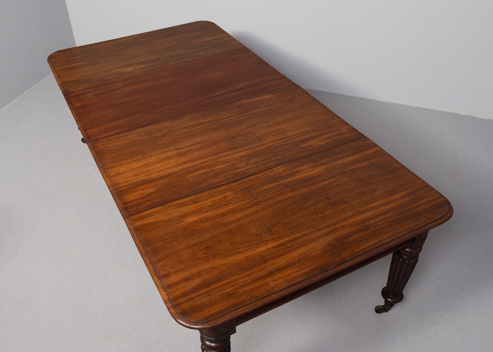 A rectangular George IV mahogany extending dining table with rounded corners, reeded turned legs, and brass castors. View IV