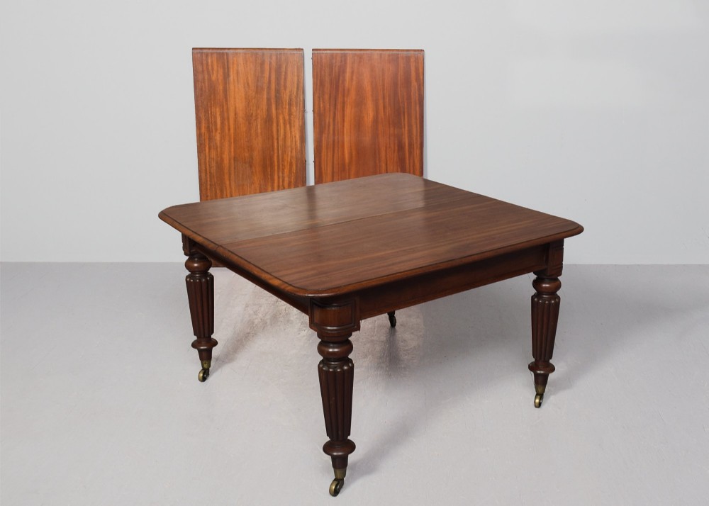 A rectangular George IV mahogany extending dining table with rounded corners, reeded turned legs, and brass castors. View V