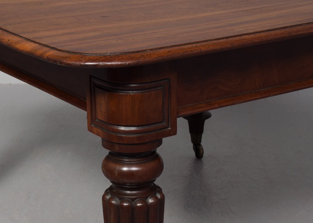 A rectangular George IV mahogany extending dining table with rounded corners, reeded turned legs, and brass castors. View VI