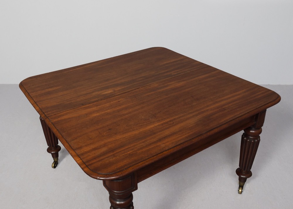 A rectangular George IV mahogany extending dining table with rounded corners, reeded turned legs, and brass castors. View VII