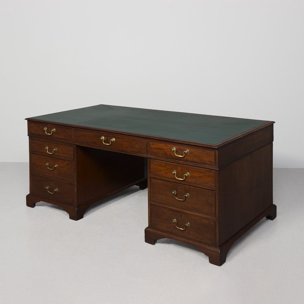 A large George III mahogany partners desk featuring a green leather writing surface, dual pedestals with brass swan-neck handles, and bracket feet.