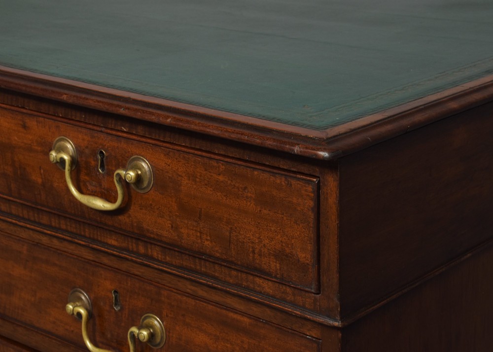 A large George III mahogany partners desk featuring a green leather writing surface, dual pedestals with brass swan-neck handles, and bracket feet. View II