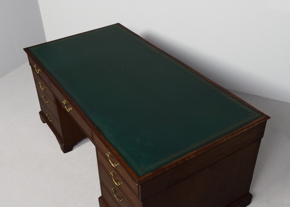 A large George III mahogany partners desk featuring a green leather writing surface, dual pedestals with brass swan-neck handles, and bracket feet. View IV